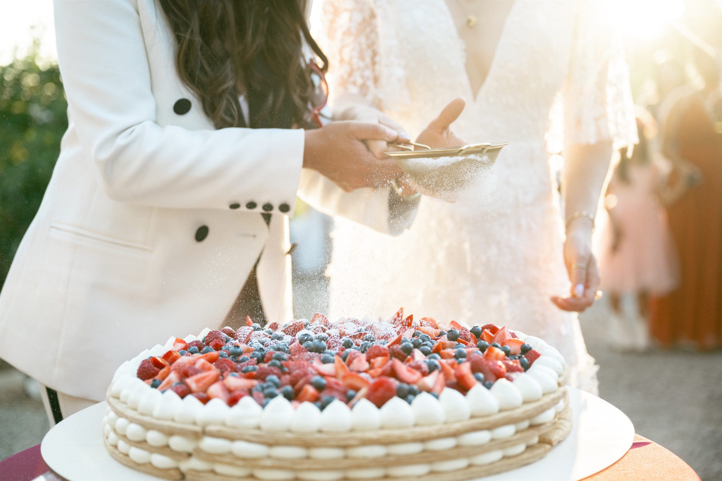 Newlyweds dusting a berry pavlova with powdered sugar at sunset