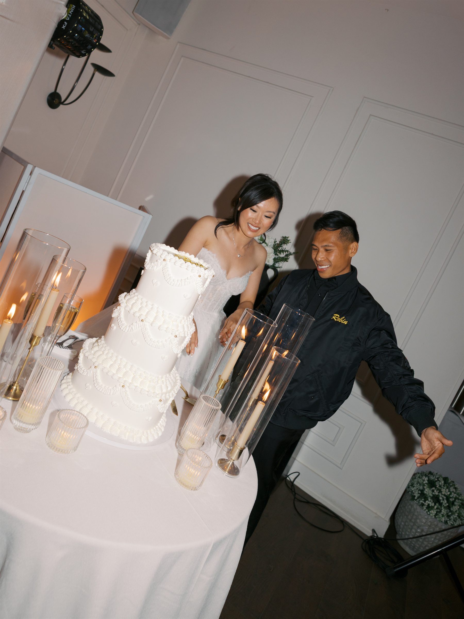 Newlyweds smiling beside their tiered wedding cake